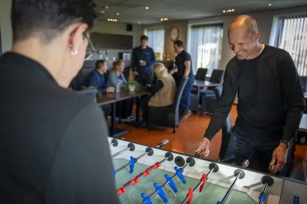 Collega's van Actemium Doetinchem ontmoeten elkaar in een informele ruimte. Op de voorgrond spelen twee collega's een potje tafelvoetbal, terwijl op de achtergrond collega's met elkaar in gesprek zijn aan een tafel. De afbeelding laat de informele en collegiale sfeer binnen Actemium zien, waar samenwerken, ontmoeten en plezier maken samenkomen.